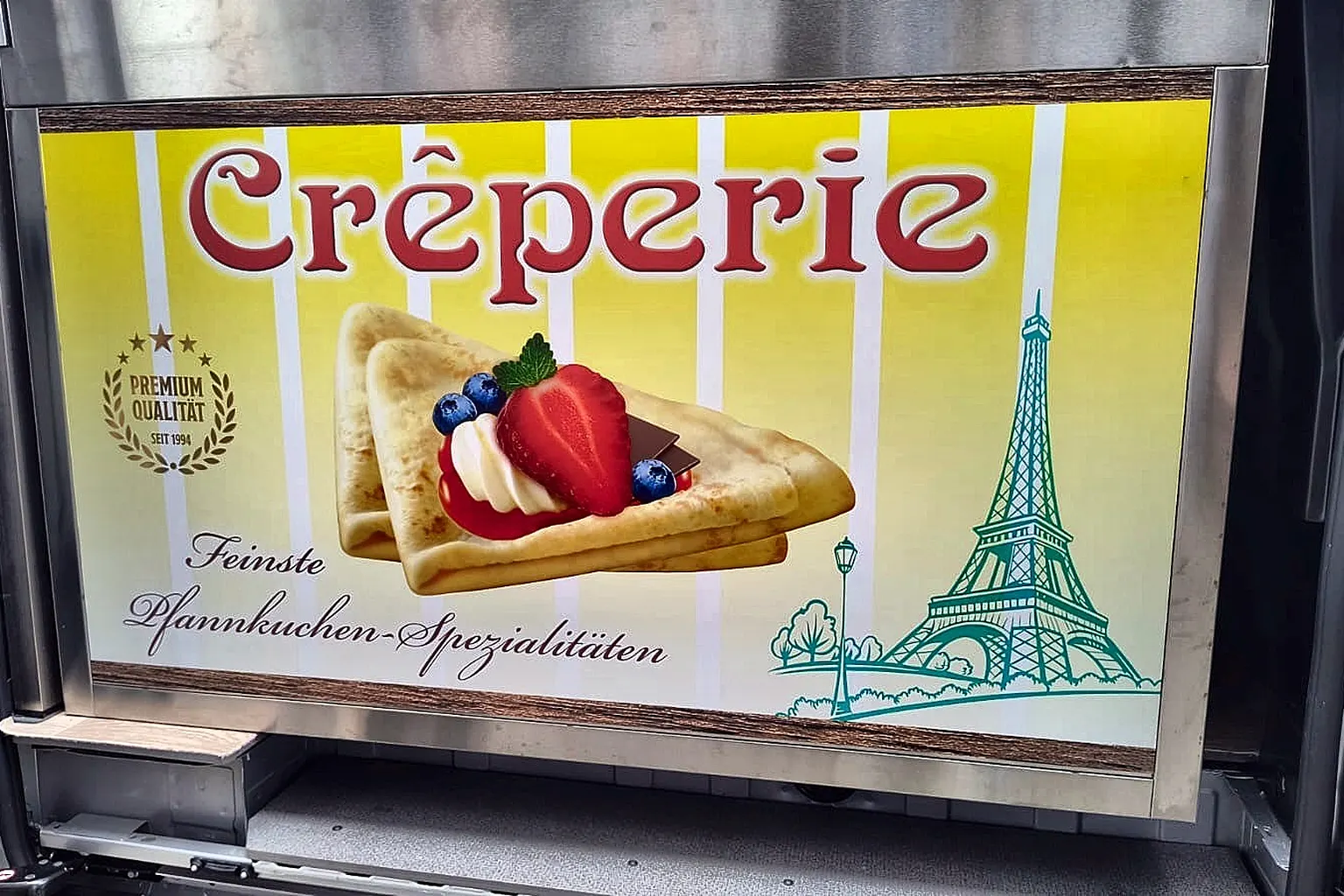 Gelbes Crêperie-Schild an der Seite des Verkaufswagens.