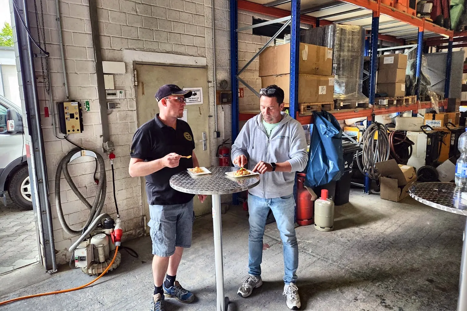 Zwei Kollegen in der Mittagspause vor den Regalen des Lagers.